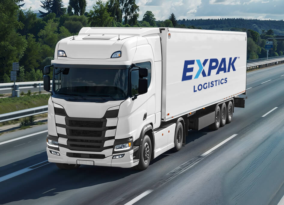 A white logistics truck with "EXPPAK LOGISTICS" branding drives on a highway surrounded by green trees under a clear blue sky.